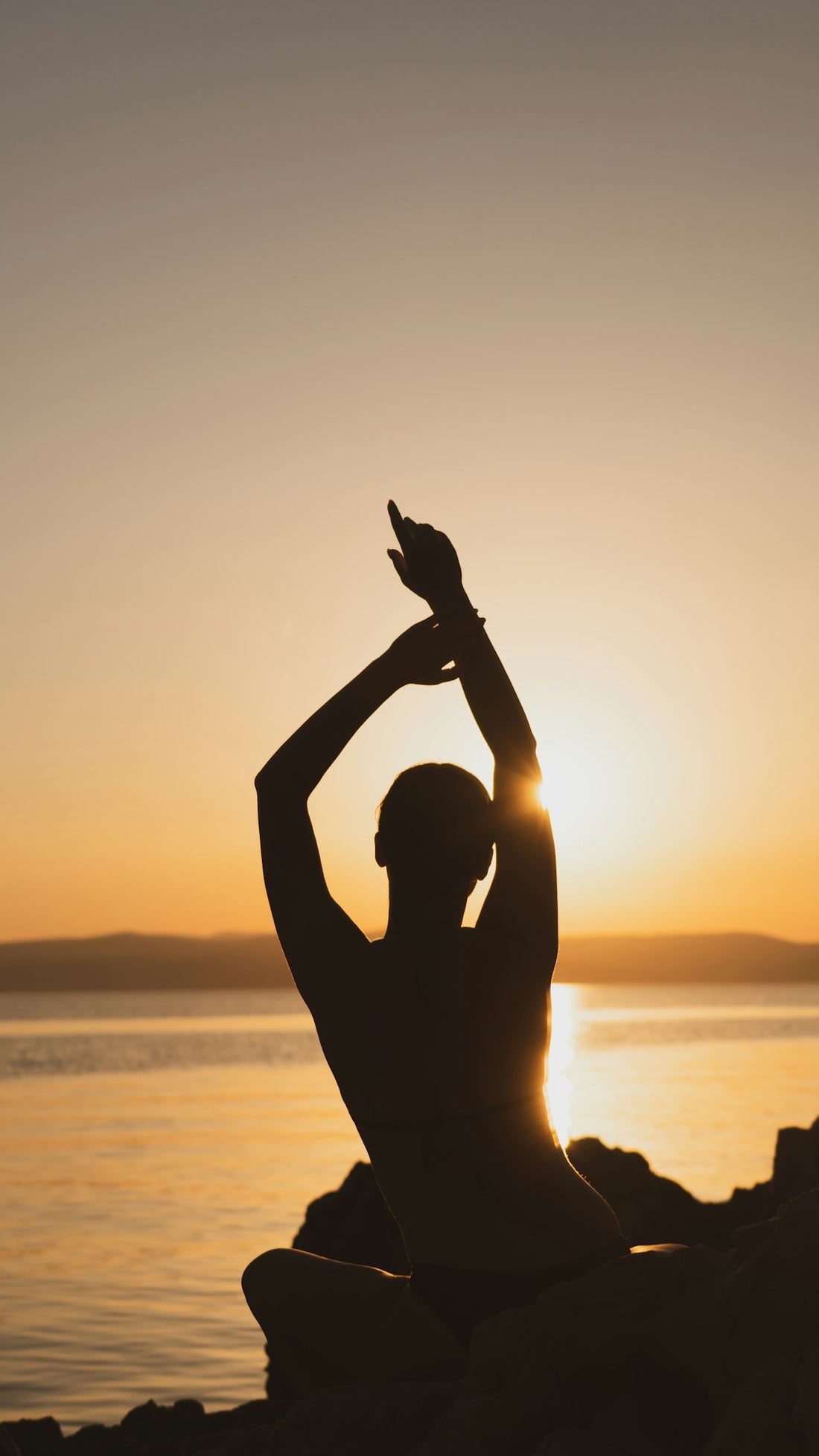Person stretching outdoors at sunset by the water
